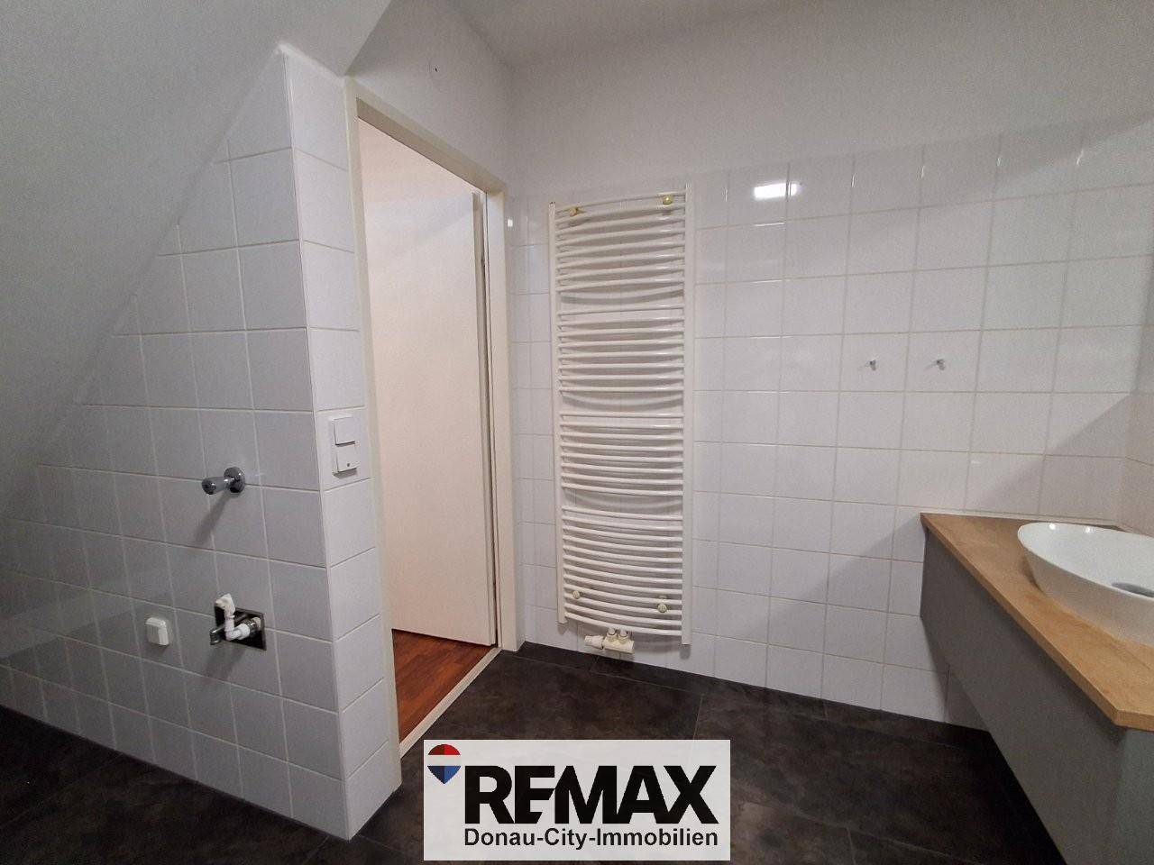 Badezimmer im Dachgeschoss mit weißen Fliesen, Waschbecken und Handtuchheizkörper unter Schrägdach.