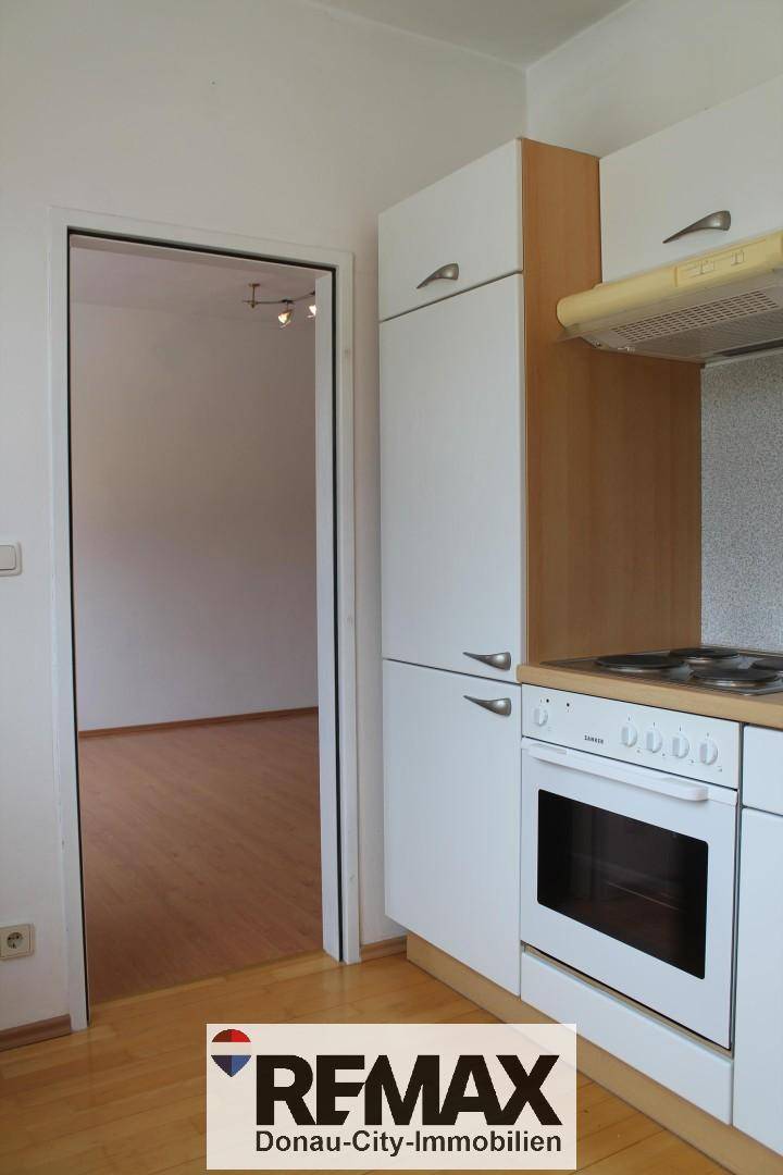 Küchenzeile mit Herd und Blick in einen angrenzenden, leeren Raum.