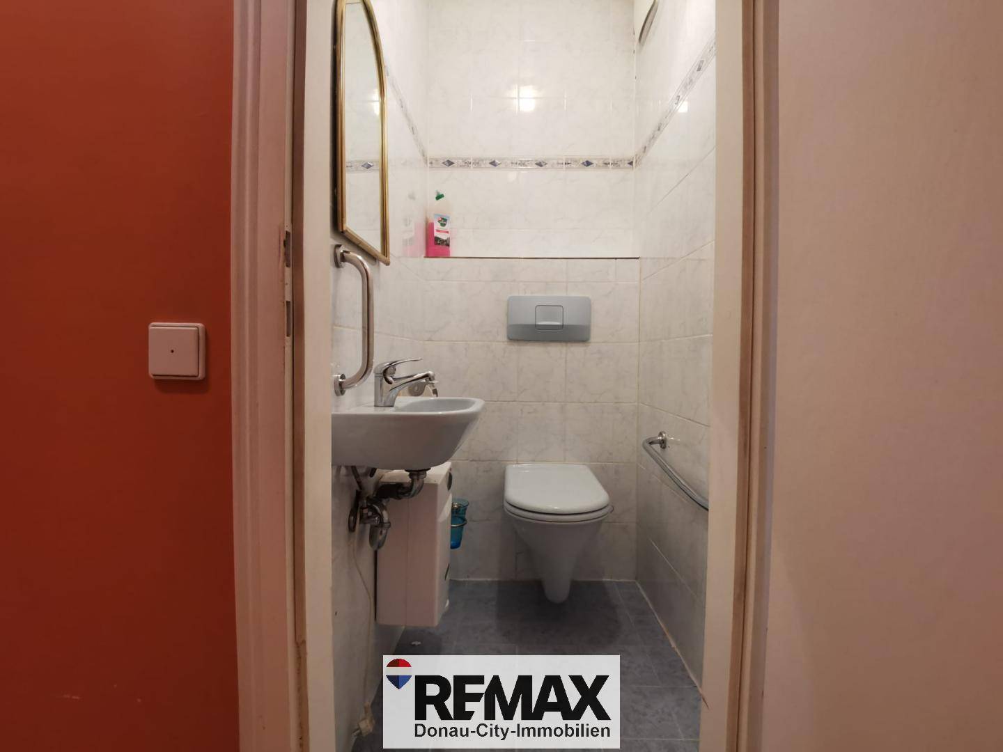 Kleines Gäste-WC mit Toilette, Waschbecken und Haltegriffen für Barrierefreiheit.