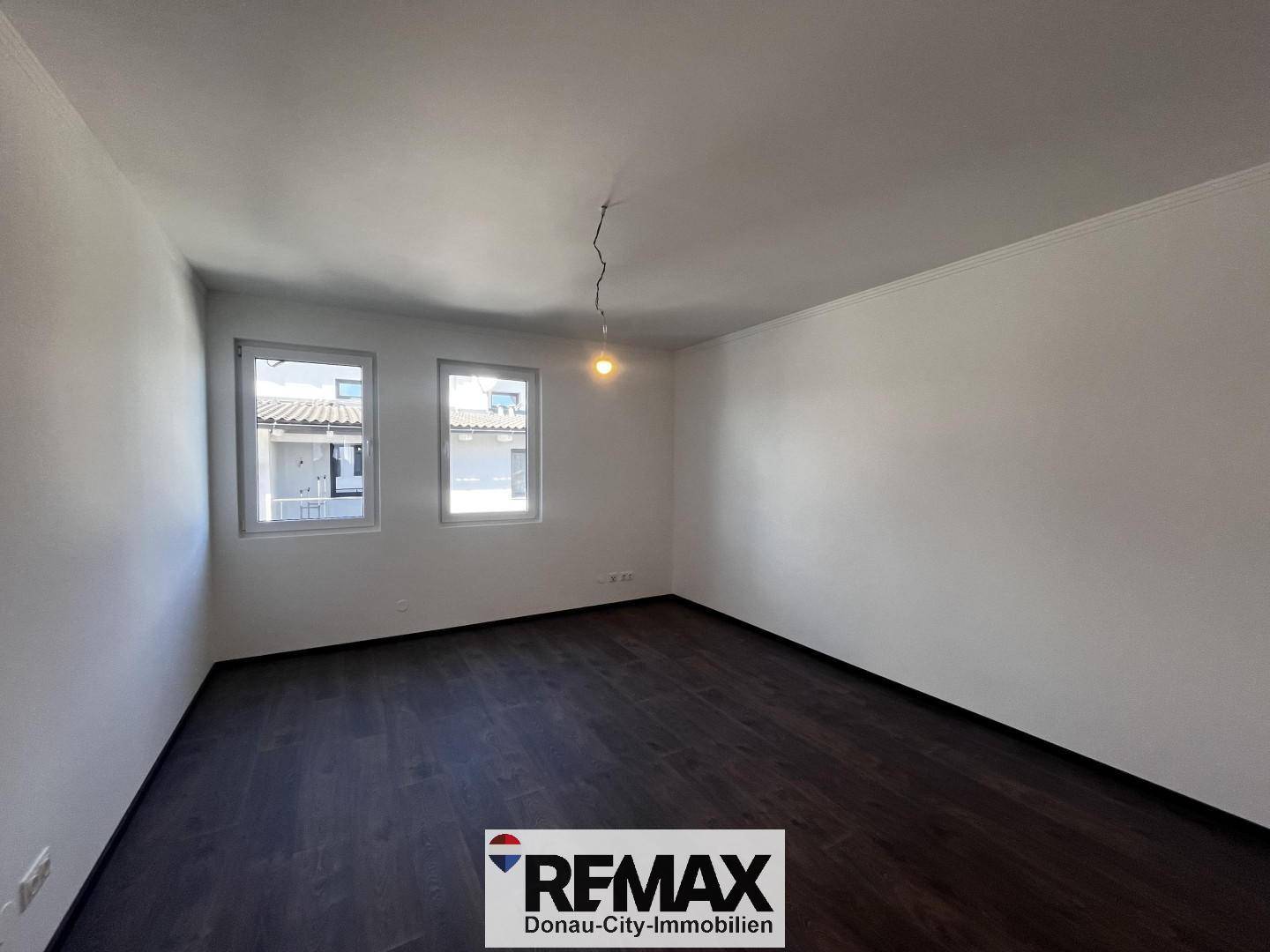 Leeres Zimmer mit zwei Fenstern und dunklem Holzboden, bereit zur individuellen Einrichtung.