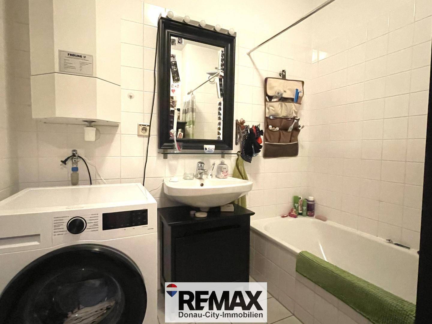 Badezimmer mit Badewanne, Waschbecken und Waschmaschine, komplett gefliest.
