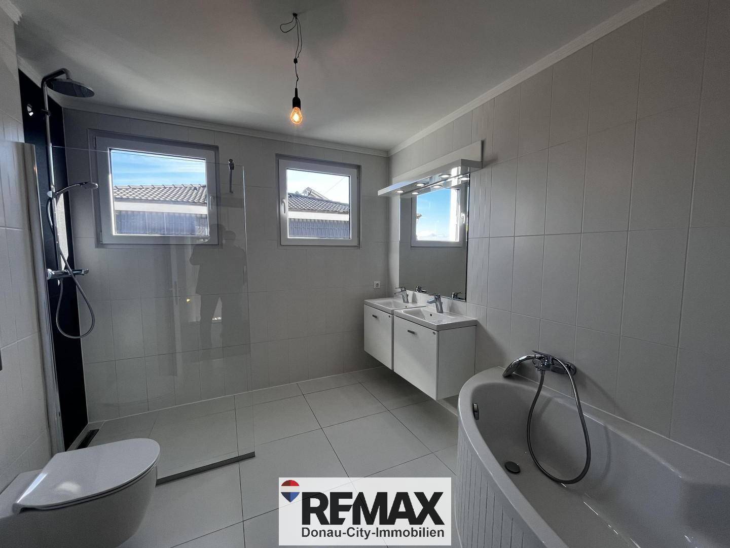 Modernes Badezimmer mit Doppelwaschbecken, Badewanne, Dusche und hellen Fliesen.