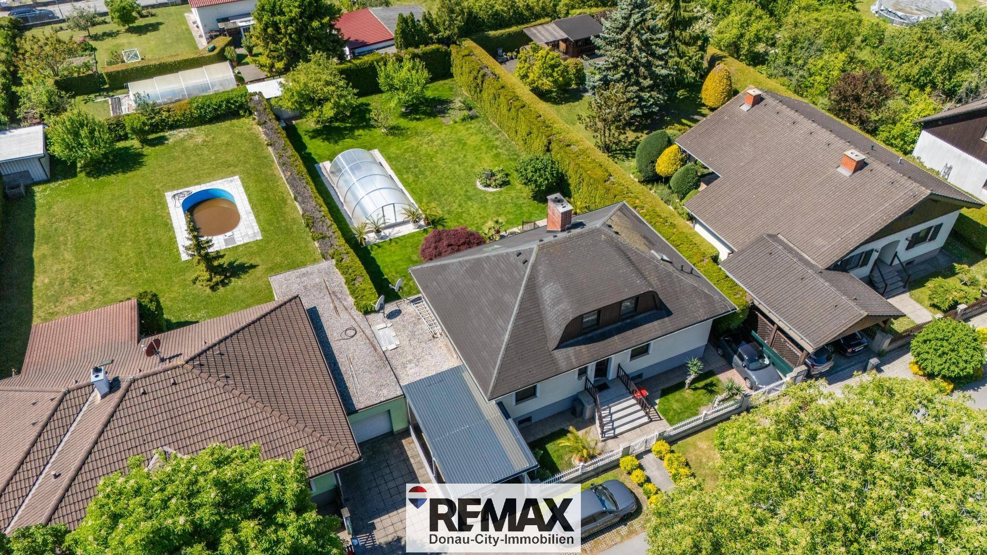 Luftaufnahme eines Wohnhauses mit Garten, Pool und umliegenden Grundstücken in grüner Umgebung.