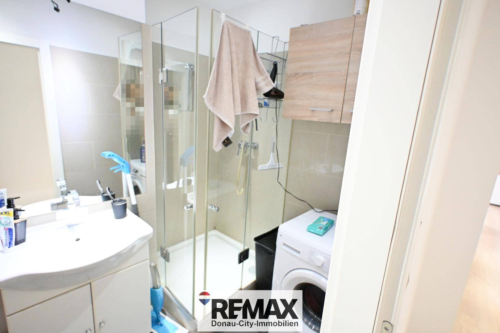 Modernes Badezimmer mit Duschkabine, Waschbecken und integrierter Waschmaschine, hell gefliest.