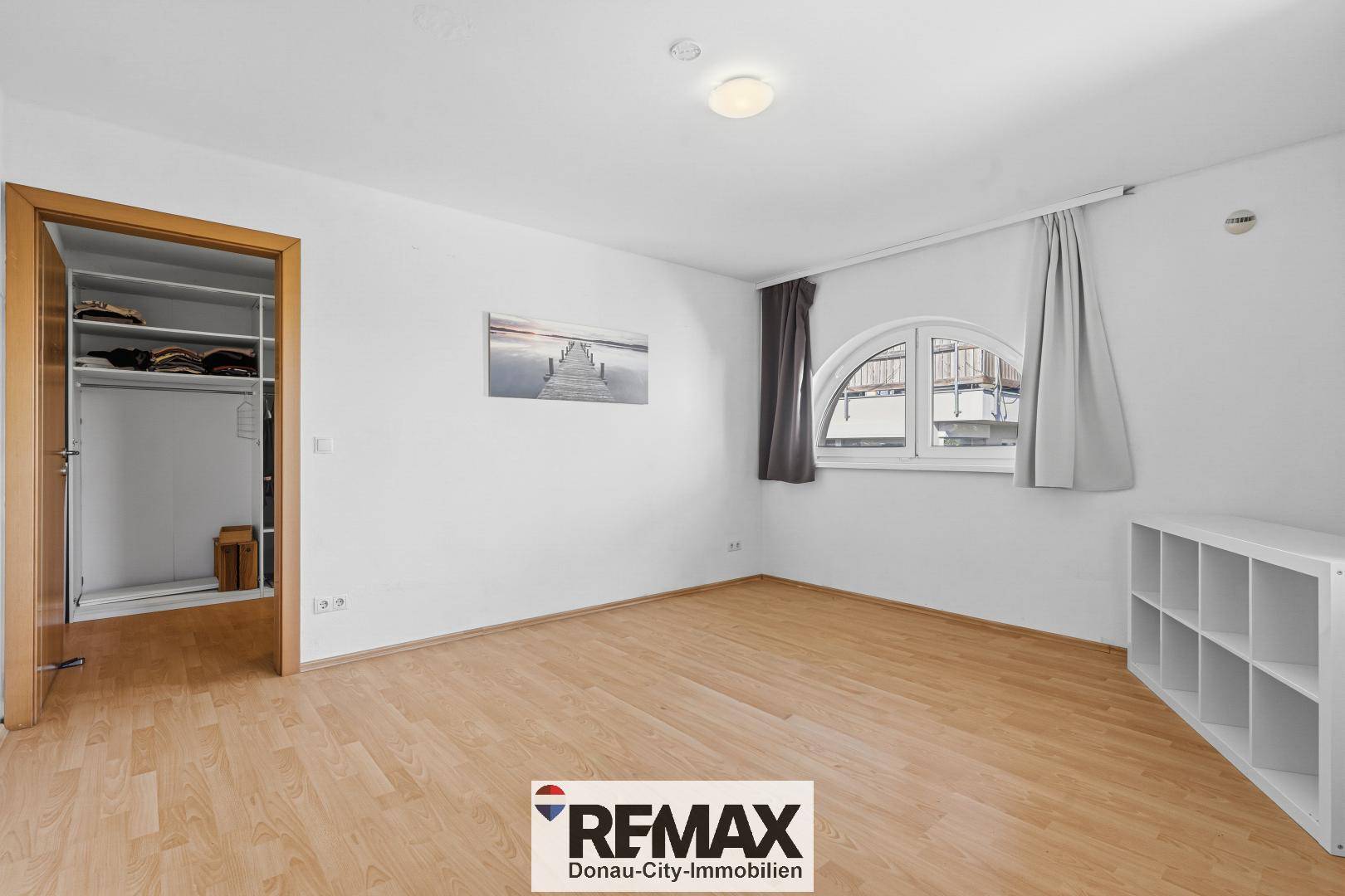 Schlafzimmer mit Holzfußboden, Einbauschrank und ungewöhnlichem Rundbogenfenster.