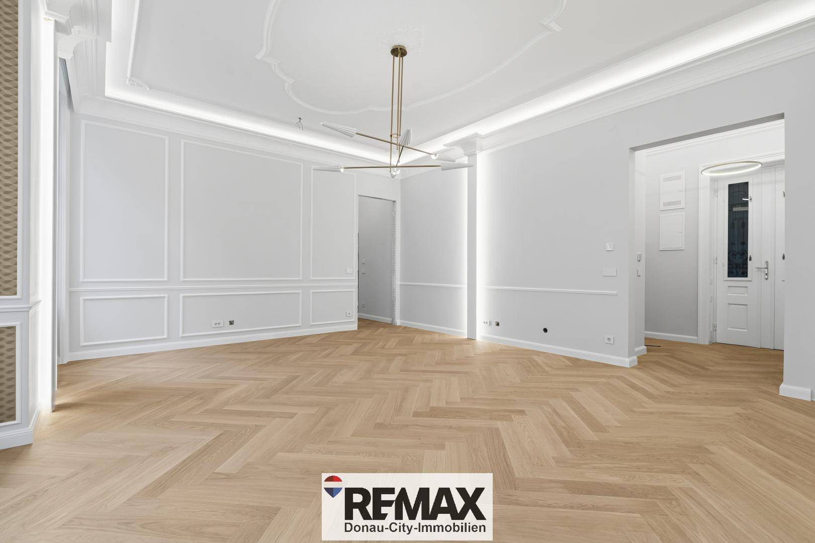 Großzügiges Wohnzimmer mit Fischgrätparkett, hohen Decken und stilvollen Wandverzierungen in einem Altbau.