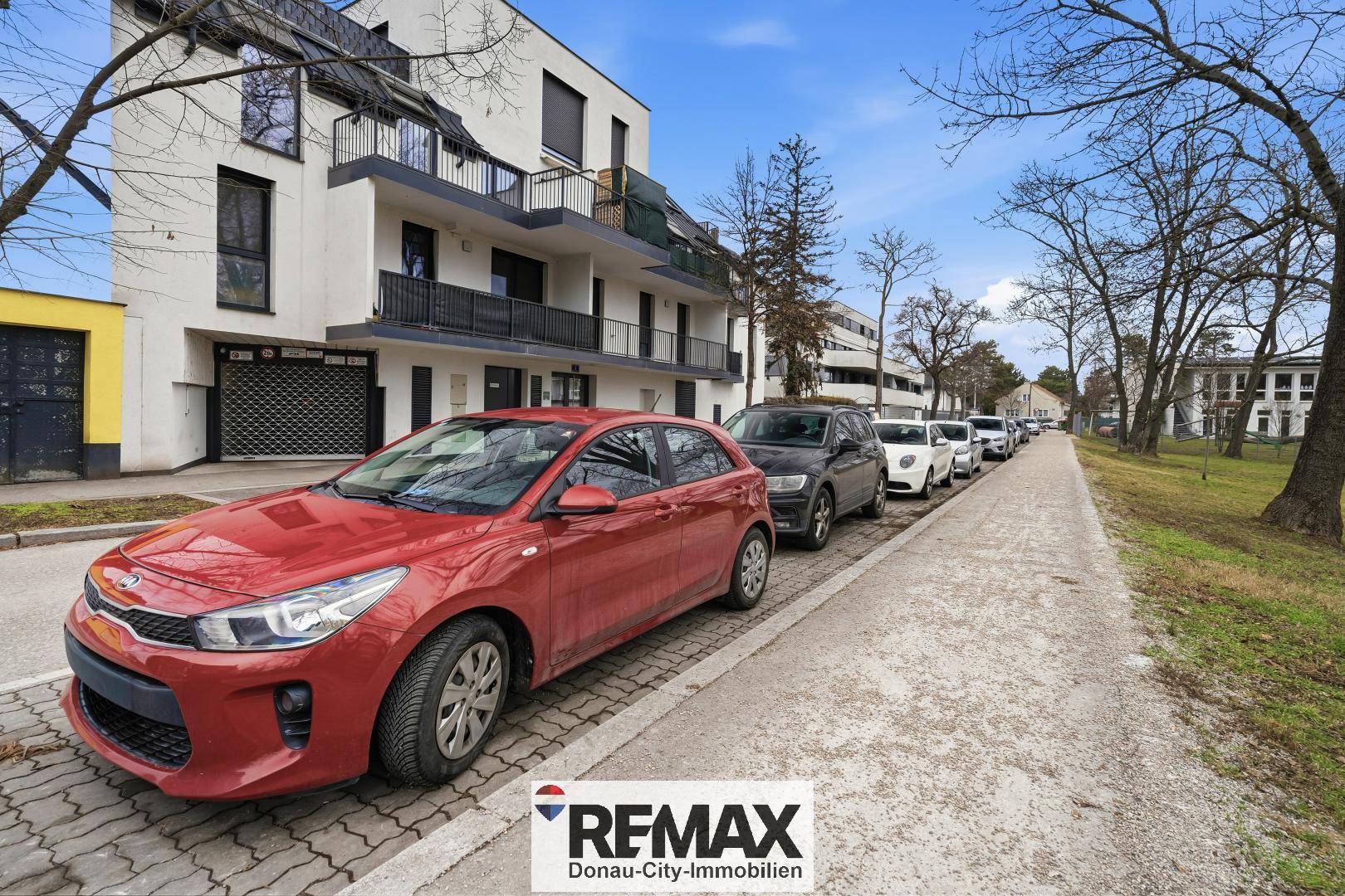 Wohngebäude an einer Straße mit parkenden Autos und Bäumen.