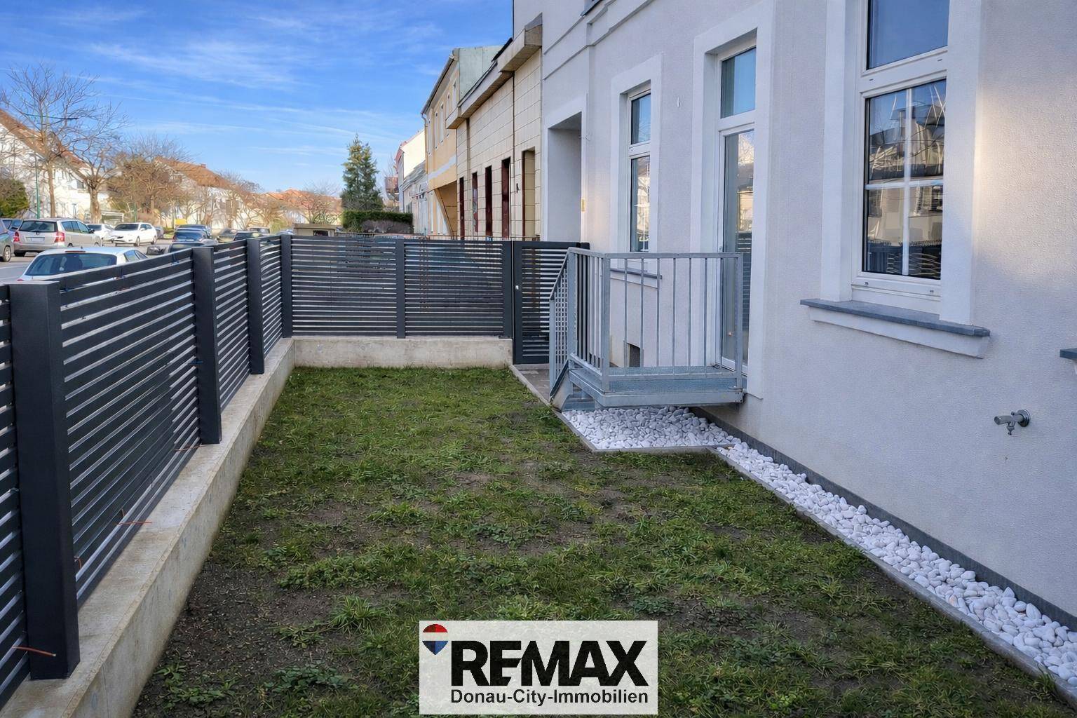 Kleiner Gartenbereich mit Rasenfläche, modernem Zaun und Zugang über eine Treppe.