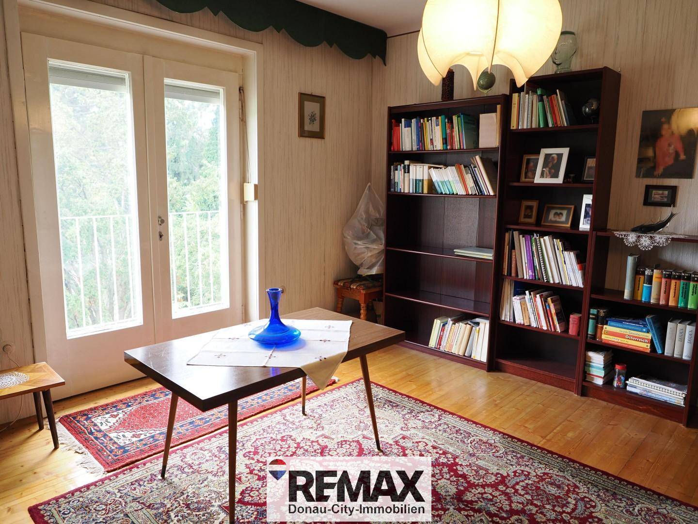 Wohnzimmer mit Bücherregalen, Holzboden und Zugang zu einem französischen Balkon.