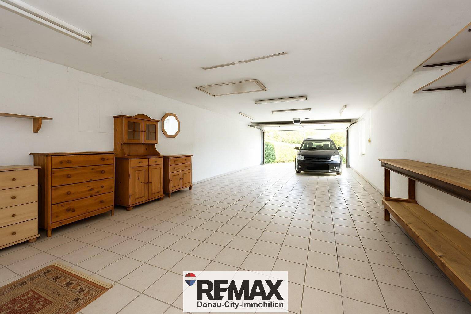 Geräumige Garage mit Fliesenboden, Regalen und einem Auto am offenen Tor.