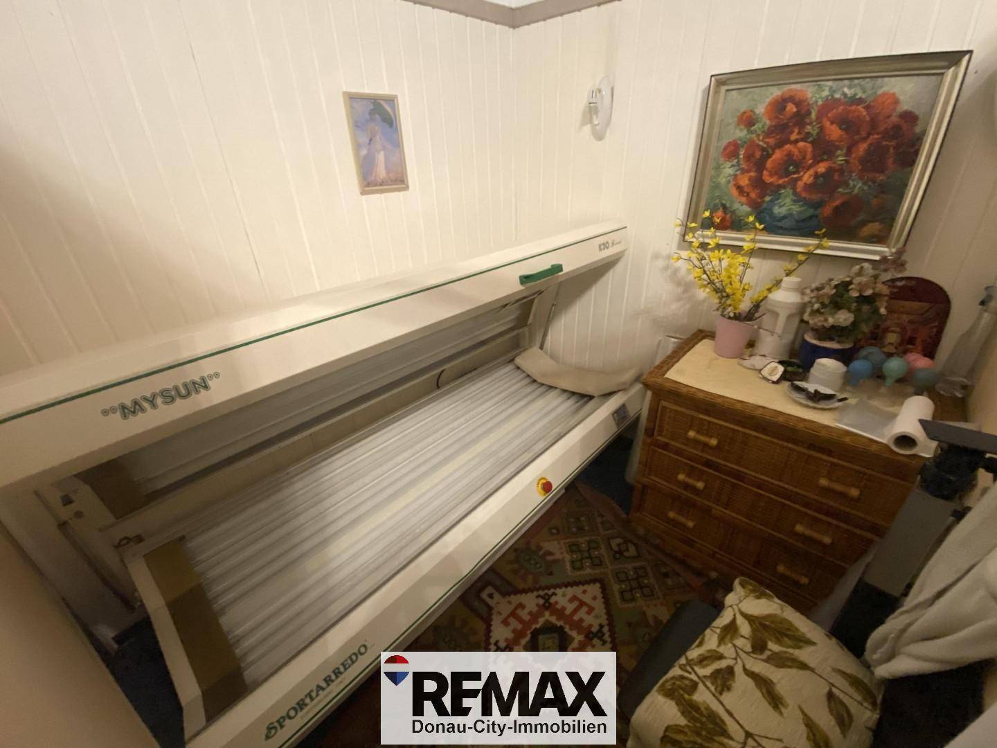 Raum mit Solarium, Holzkommode und gerahmtem Bild an der Wand.