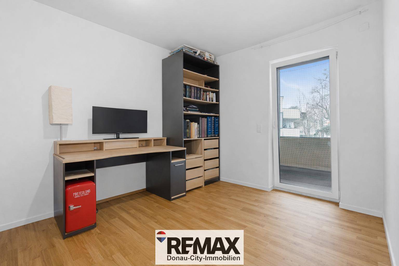 Arbeitszimmer mit Schreibtisch, Bücherregal und Zugang zu einem Balkon.