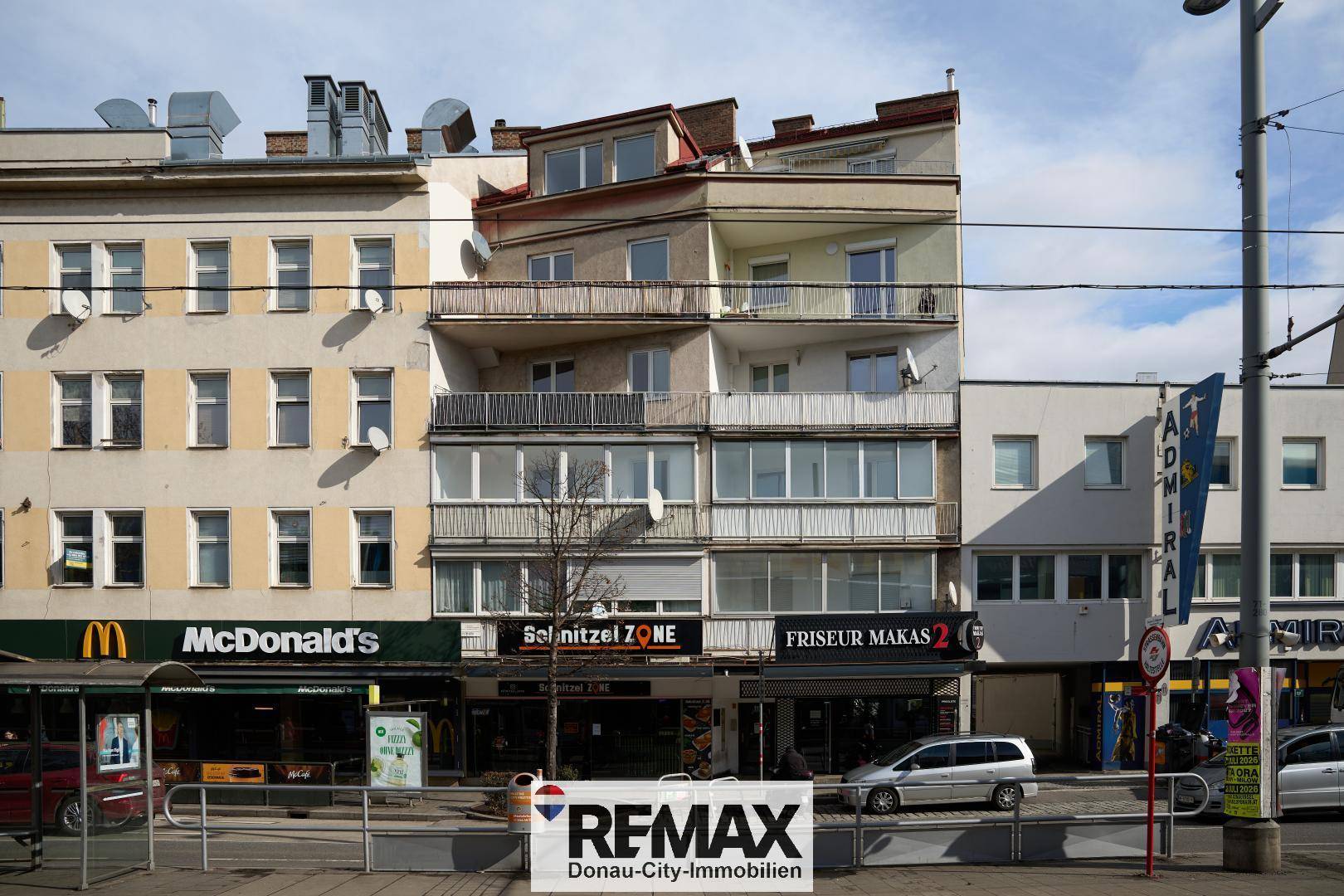 Mehrstöckiges Gebäude mit Geschäften im Erdgeschoss an einer belebten Stadtstraße.