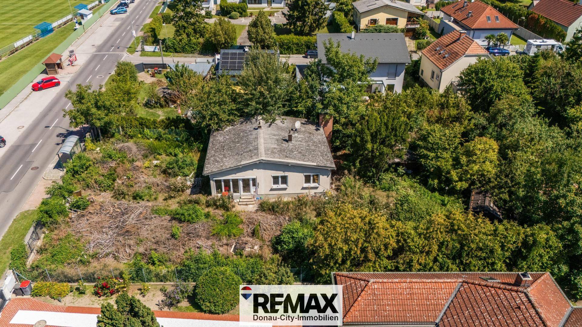 Luftaufnahme des Grundstücks mit einem kleinen Haus und viel Bewuchs, angrenzend an eine Straße.