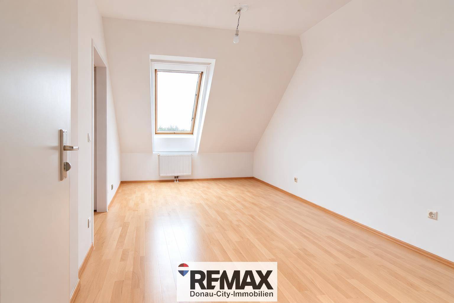 Leeres Schlafzimmer mit Holzboden, Dachschräge und einem Dachfenster für natürliches Licht.