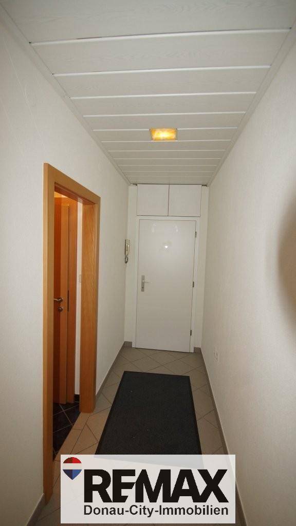 Heller Flur mit weißer Tür und Deckenbeleuchtung, führt zu weiteren Räumen.