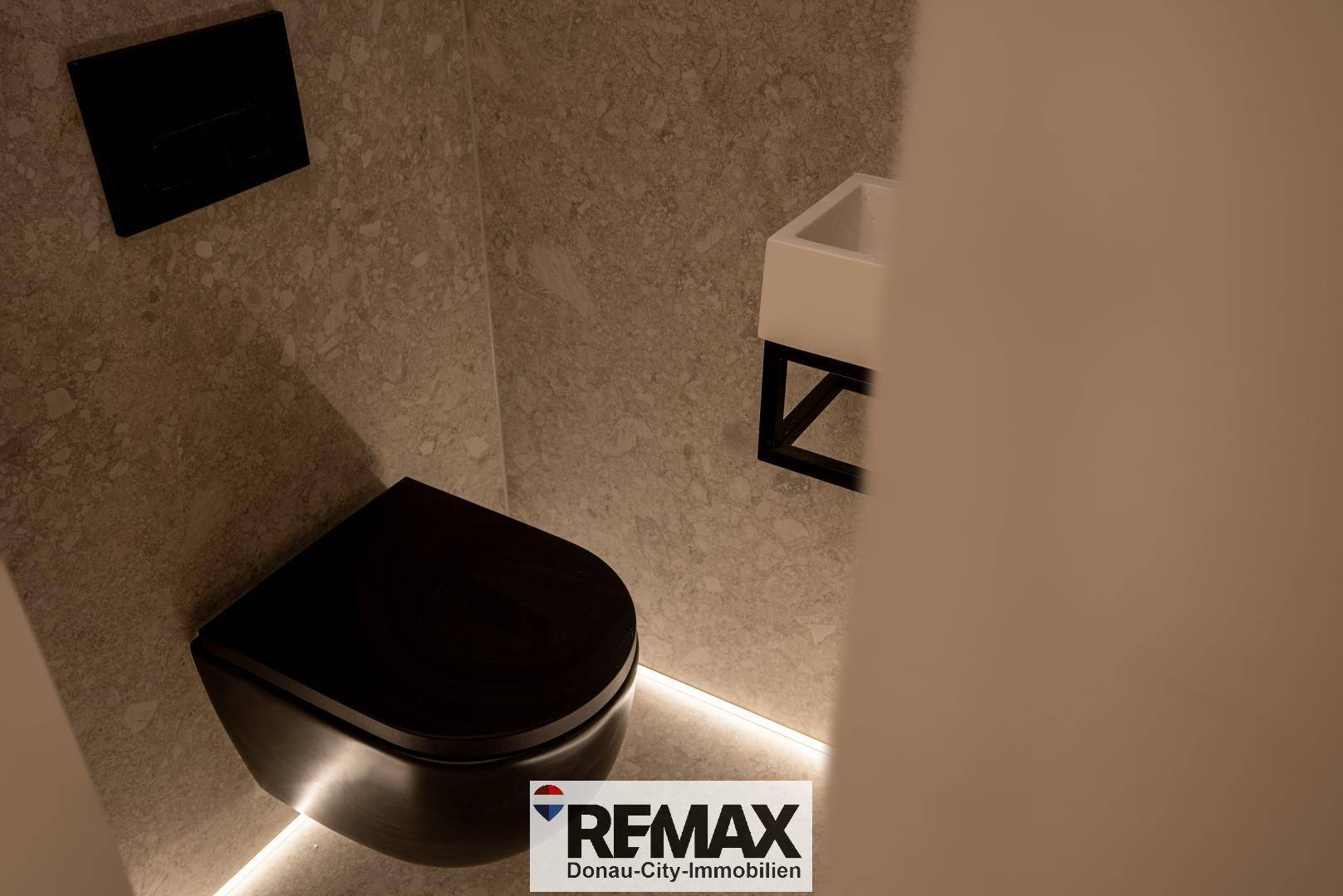 Separates WC mit schwarzer Wandtoilette und kleinem Waschbecken, modern gestaltet.