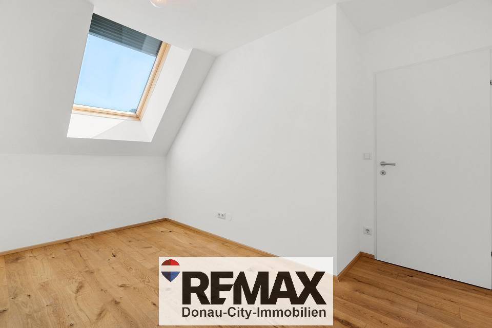 Zimmer mit Holzboden, weiß gestrichenen Wänden und einem Dachfenster mit integriertem Rollo.