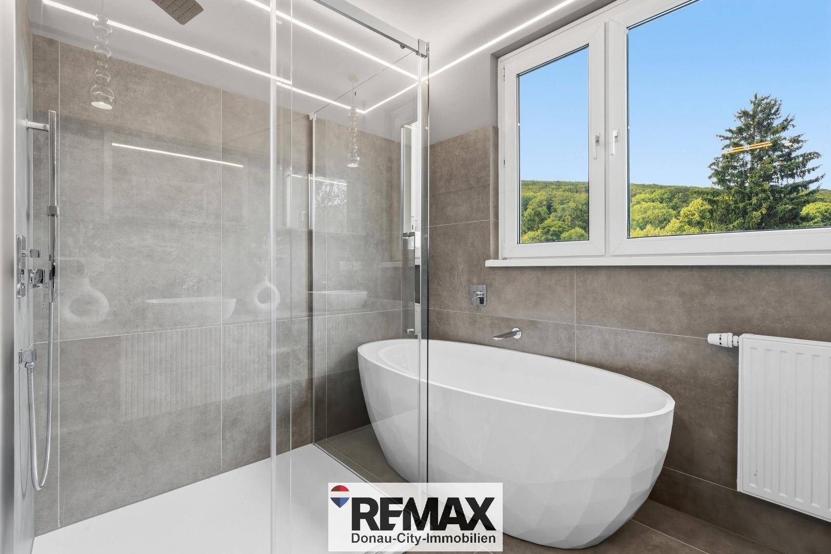 Modernes Badezimmer mit freistehender Badewanne, großer Dusche und Fenster mit Grünblick.