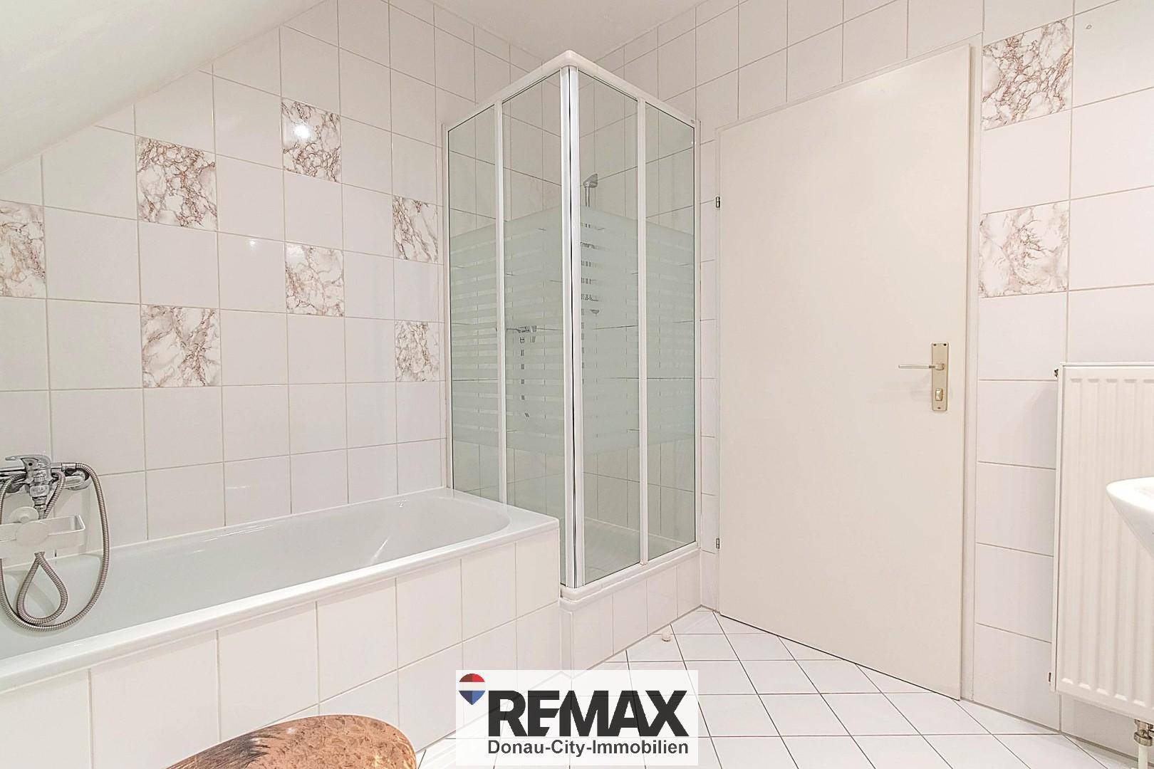 Badezimmer mit Badewanne, Duschkabine und Dachschräge, ausgestattet mit weißen Fliesen und Marmor-Akzenten.