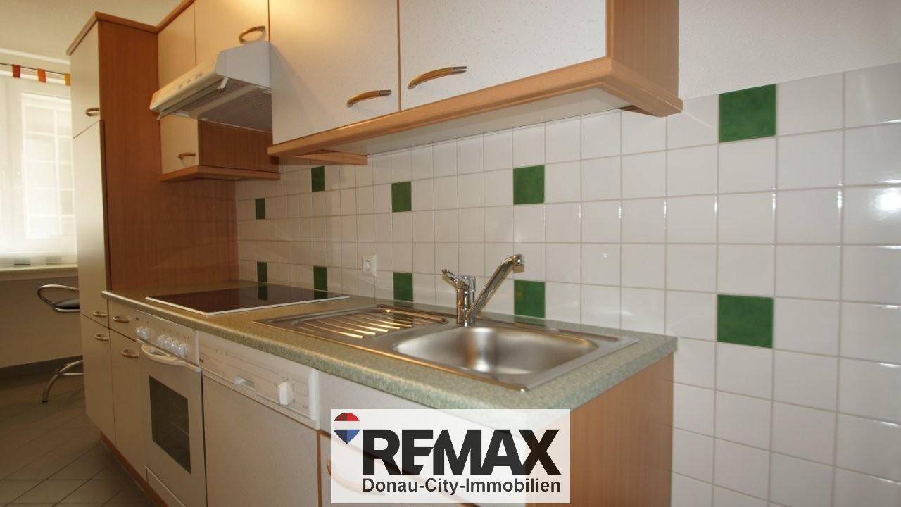 Funktionale Küche mit weißen Schränken, integriertem Backofen und Essbereich am Fenster.