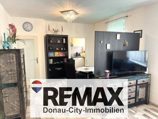 Wohnzimmer mit Fernseher, dekorativem Schrank und Blick in die angrenzende Küche.