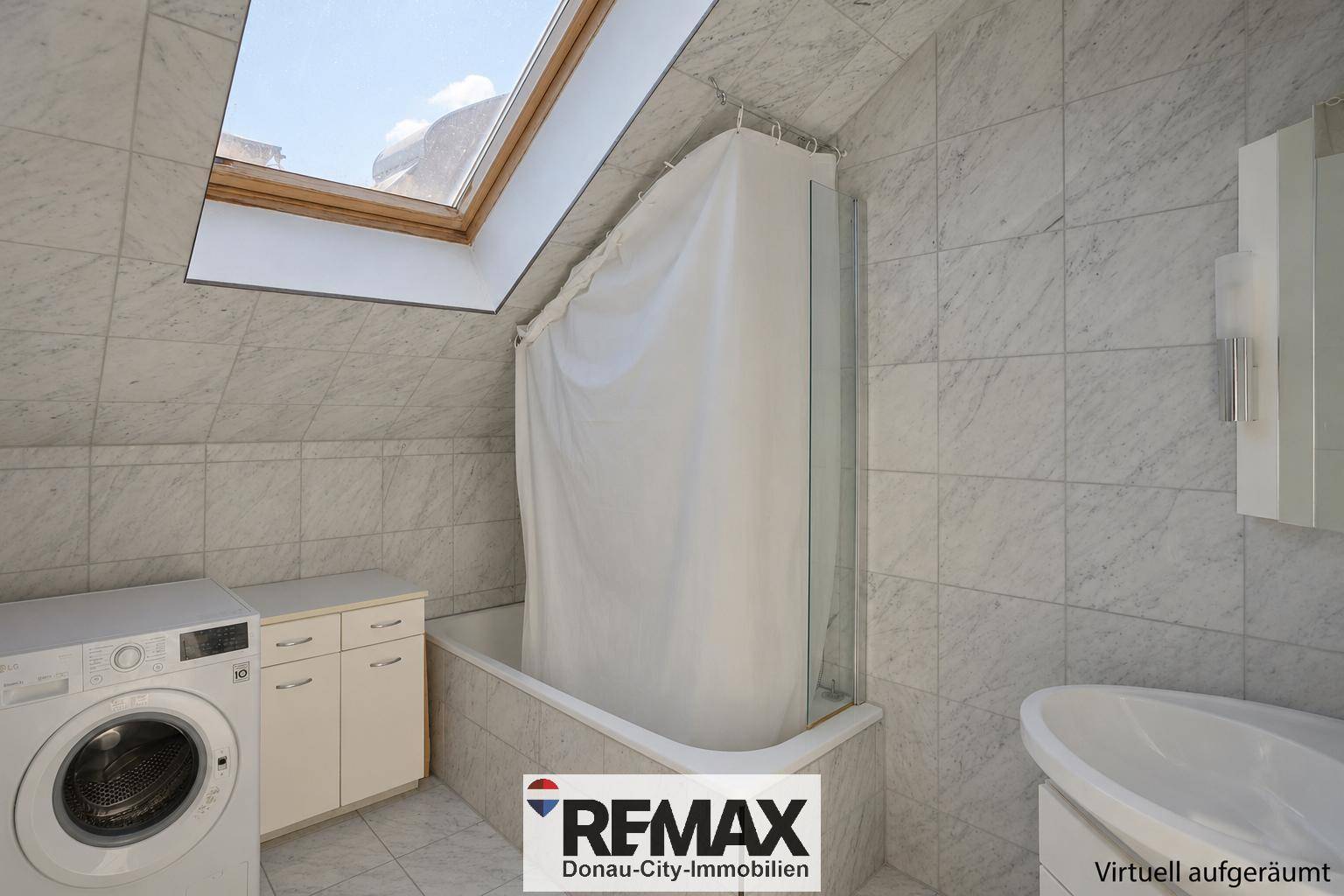 Badezimmer mit Badewanne, Waschmaschine und Waschbecken unter einem Dachfenster in gefliestem Raum.