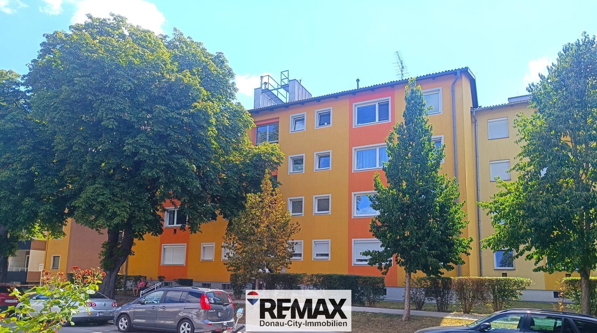 Mehrfamilienhaus mit farbiger Fassade und Bäumen an der Straße.