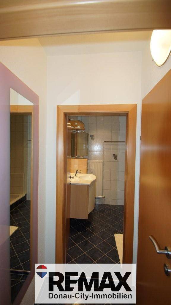 Flur mit Zugang zu einem Badezimmer, das Waschbecken und Spiegel zeigt.