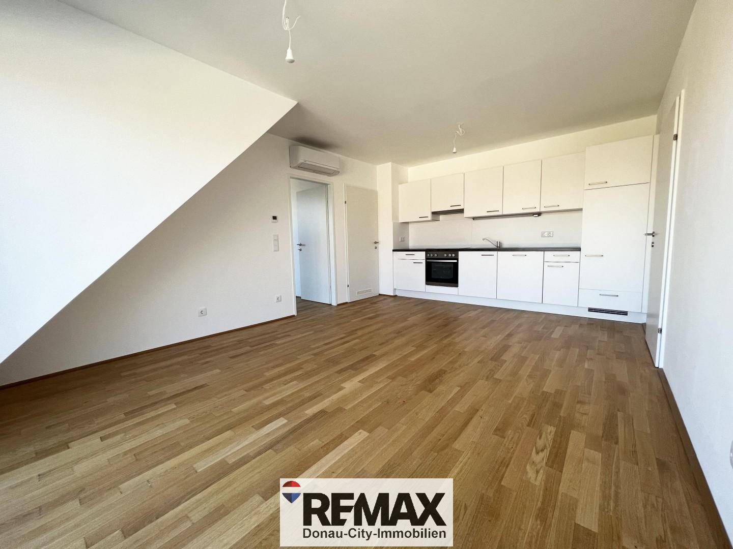 Heller, unmöblierter Wohnbereich mit Einbauküche, Holzboden und Dachschräge.