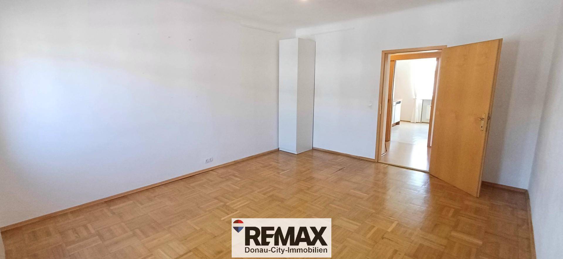 Geräumiger Innenraum mit Parkettboden und einer Tür, die zu einem weiteren Zimmer führt.