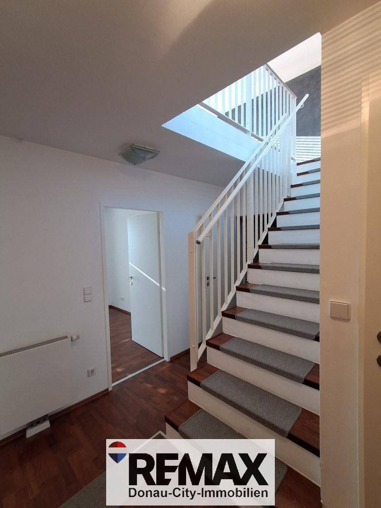 Heller Flur mit Holztreppe und dunklem Laminatboden, der die oberen Etagen verbindet.