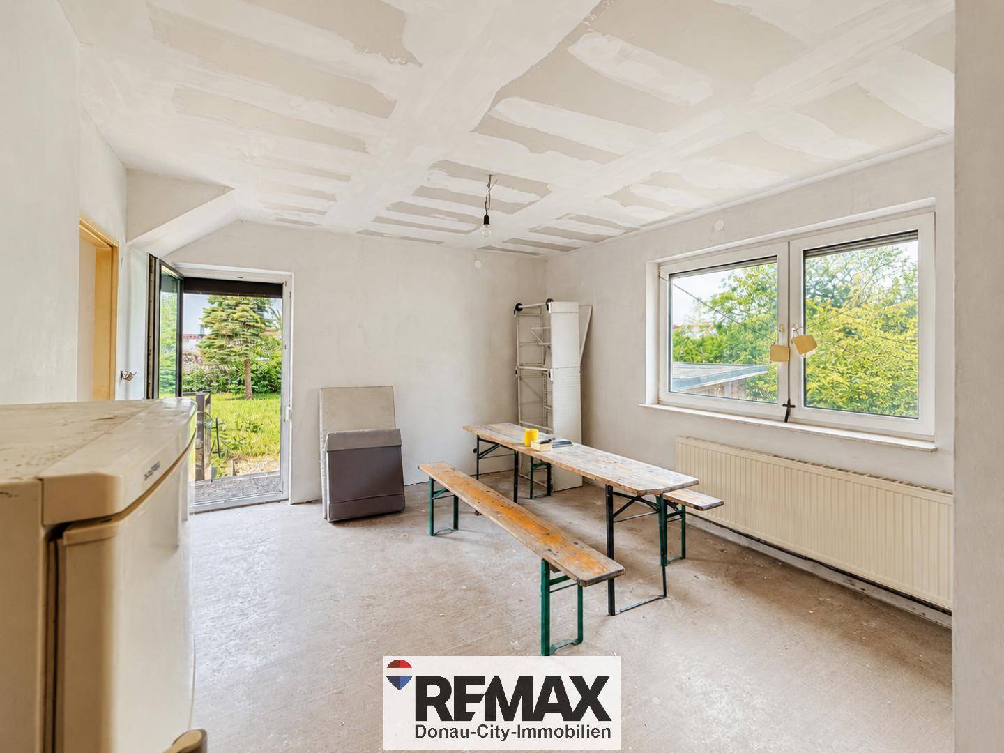 Renovierungsbedürftiger Raum mit provisorischen Bänken und Blick in den Garten.
