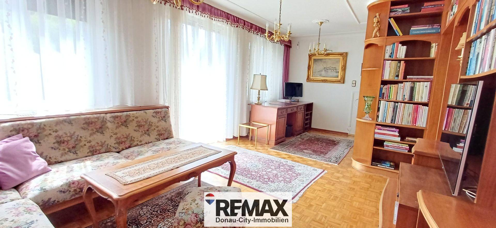 Geräumiges Wohnzimmer mit Sofa, Schreibtisch und großen Fenstern für viel Tageslicht.