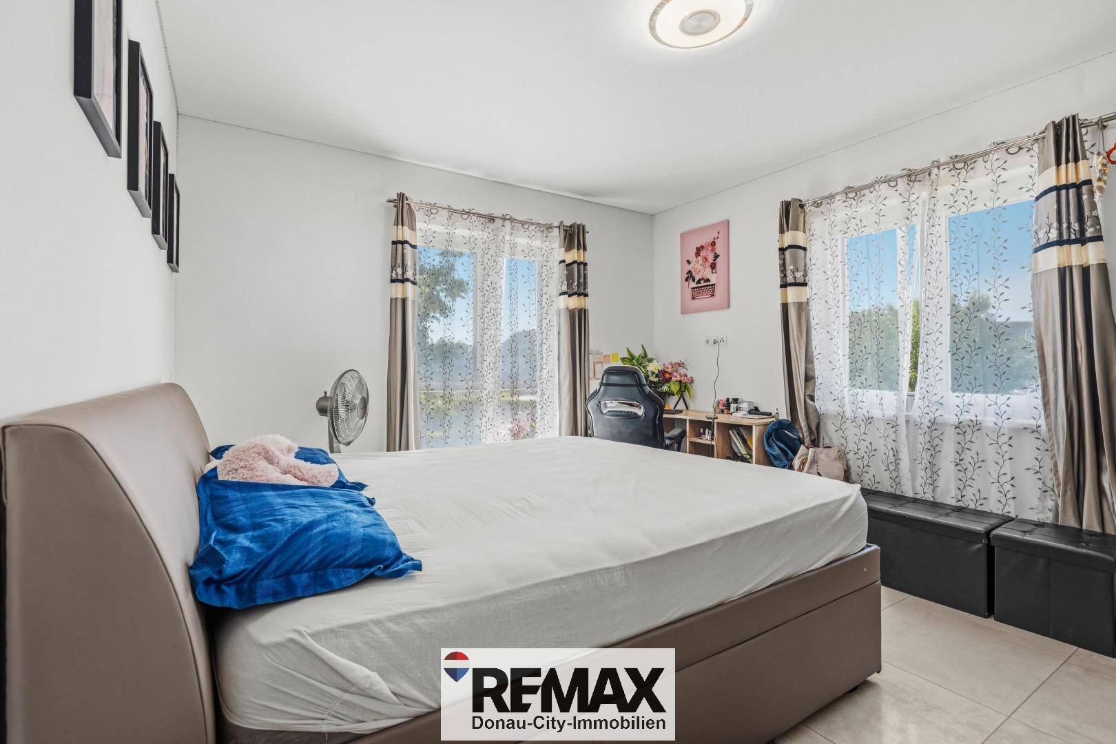 Helles Schlafzimmer mit großem Bett, Fliesenboden und Blick ins Grüne durch die Fenster.