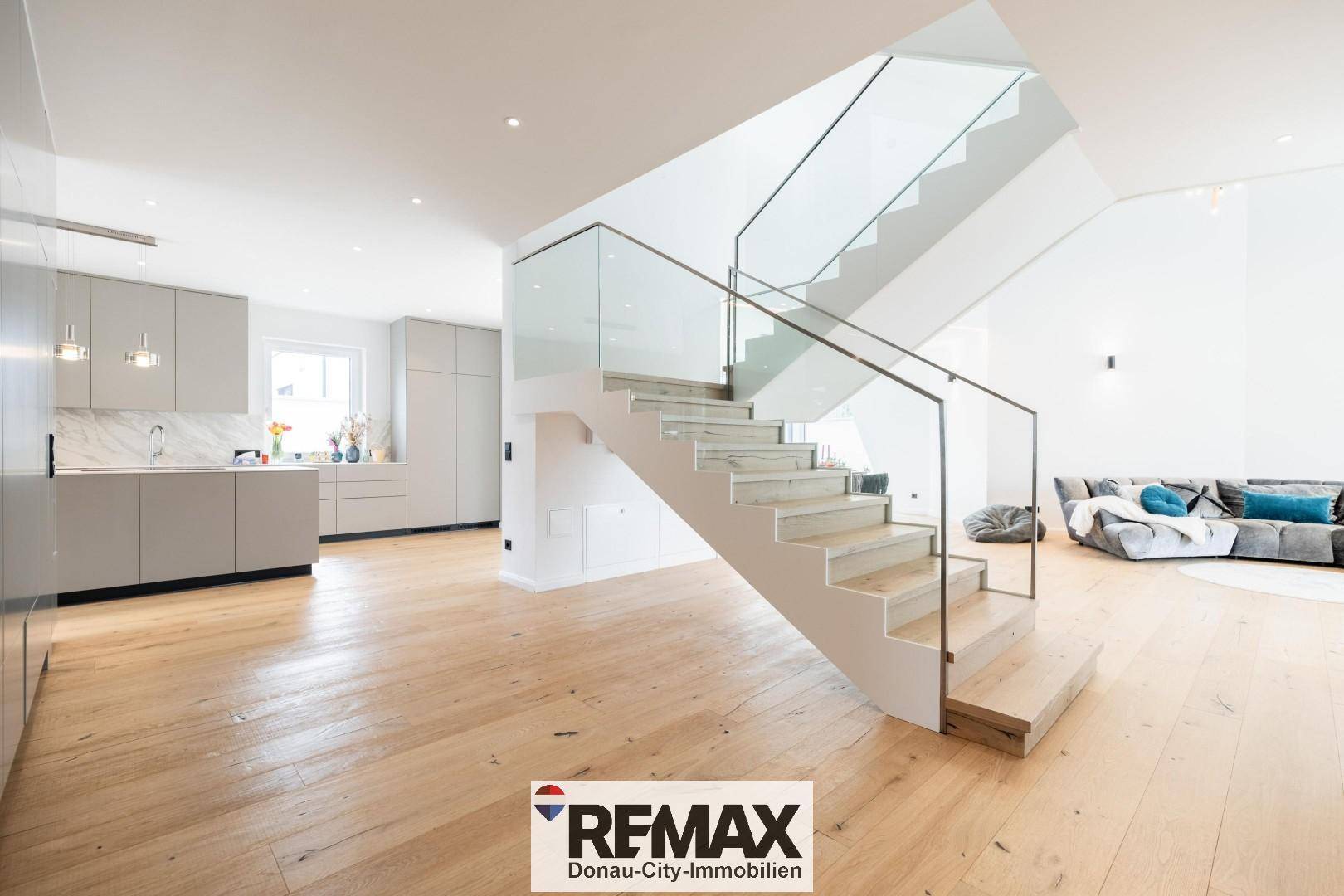 Offener Wohn- und Essbereich mit integrierter Küche und moderner Treppe mit Glasgeländer.