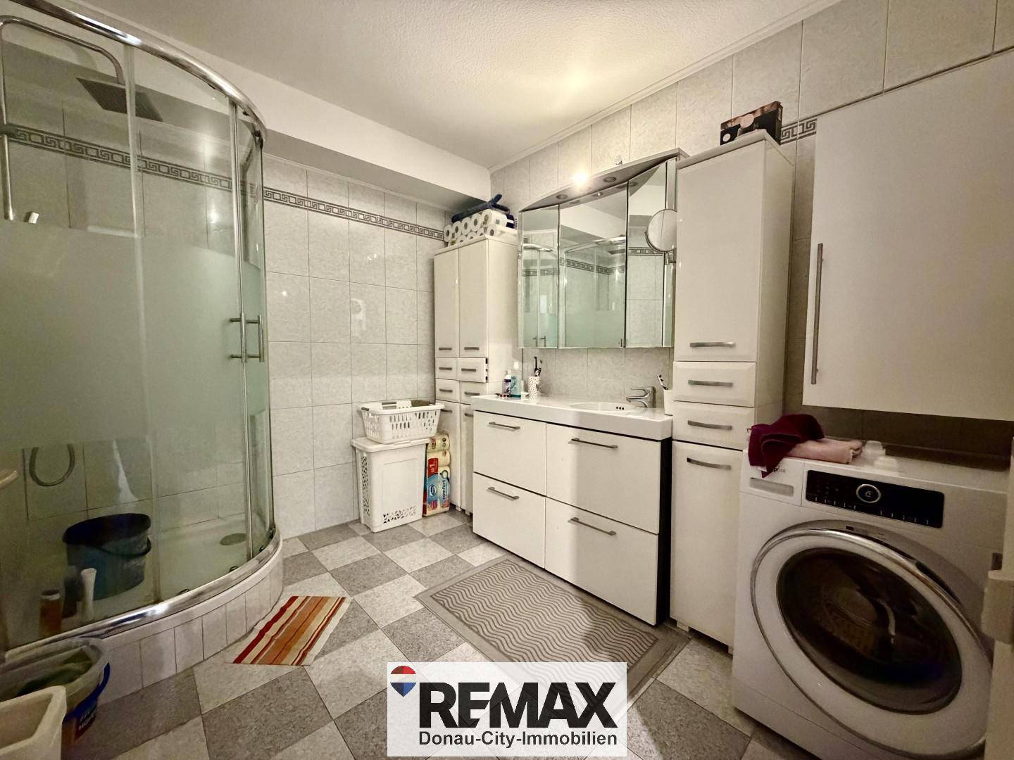 Badezimmer mit Duschkabine, Waschbecken, Spiegelschrank und Waschmaschine.