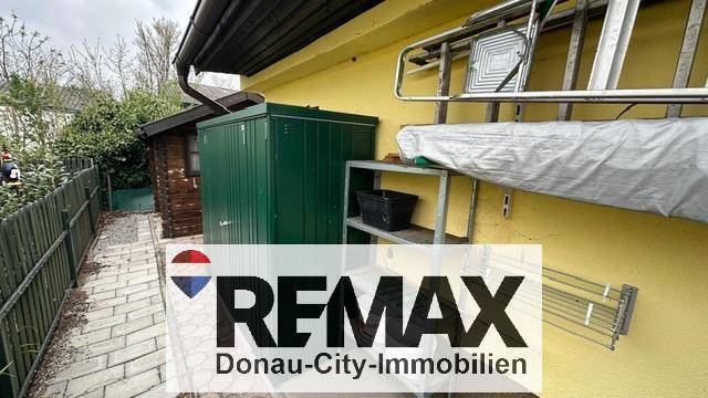 Seitenansicht eines gelben Gebäudes mit grünem Abstellschrank und Holzschuppen.