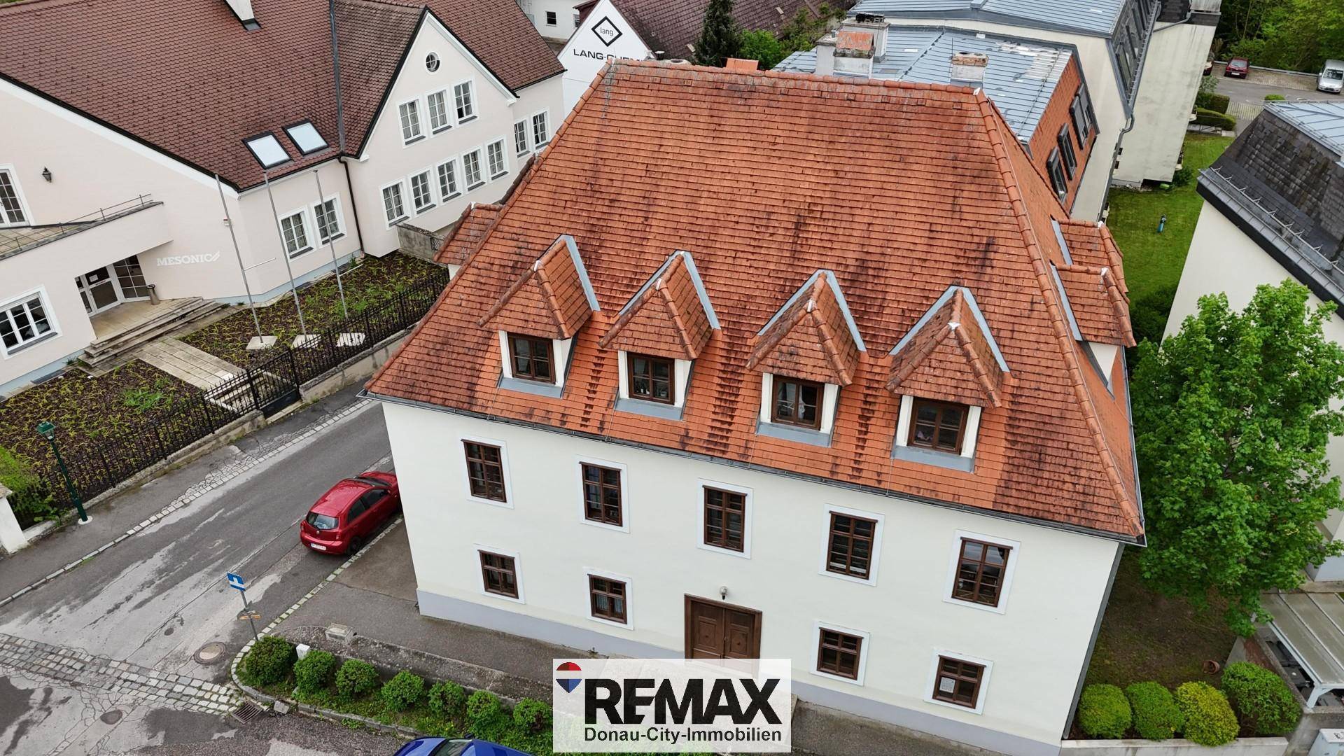 Luftaufnahme des historischen Gebäudes mit umliegender Bebauung und Straße.