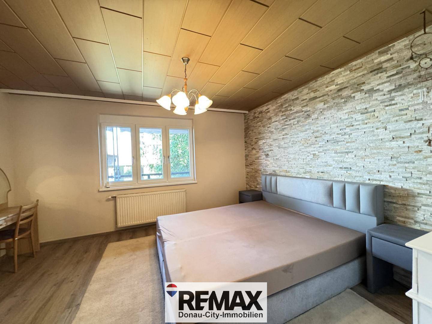 Schlafzimmer mit Doppelbett, Steinwandakzent und Holzdeckenverkleidung, bietet eine gemütliche Atmosphäre.