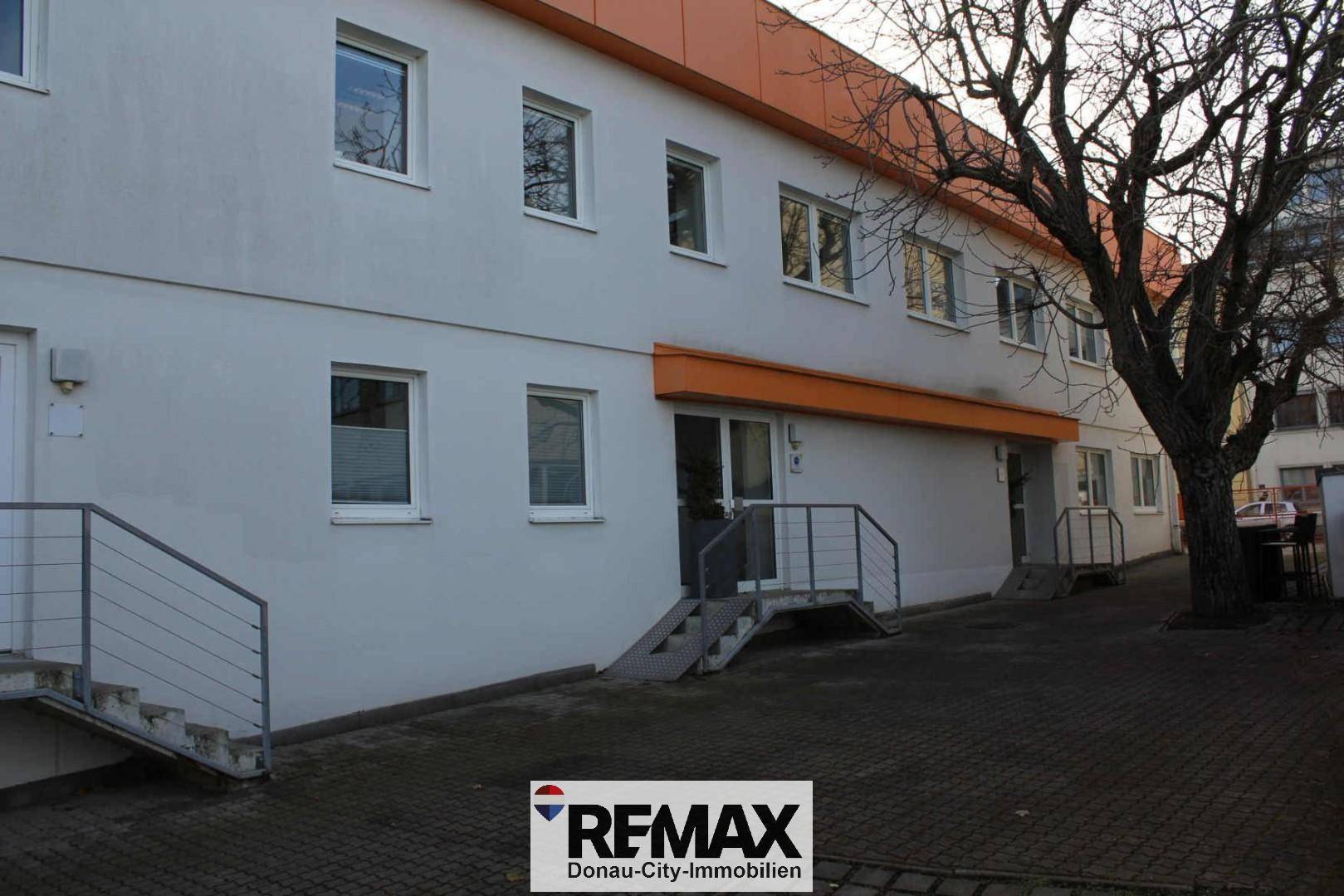 Außenansicht eines Geschäftsgebäudes mit weißer Fassade, orangefarbenen Akzenten und barrierefreiem Zugang.