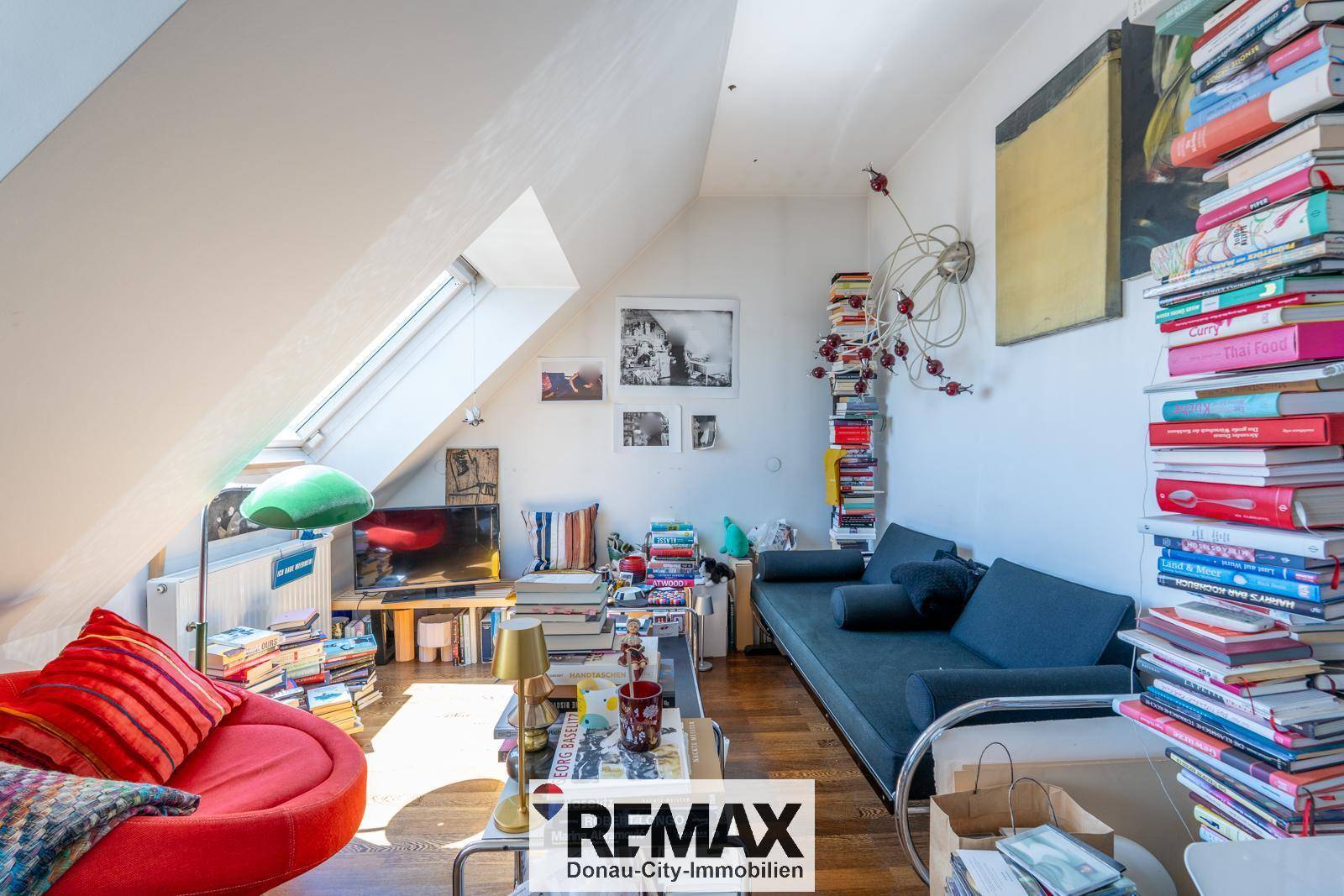 Gemütliches Wohnzimmer im Dachgeschoss mit vielen Büchern, Holzboden und natürlichem Licht durch Dachfenster.