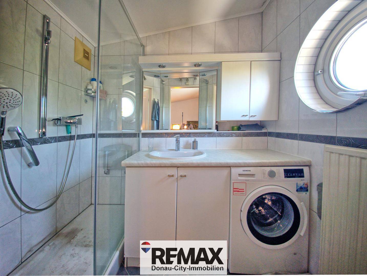 Helles Badezimmer mit Dusche, Waschbecken und Waschmaschine unter dem Fenster.