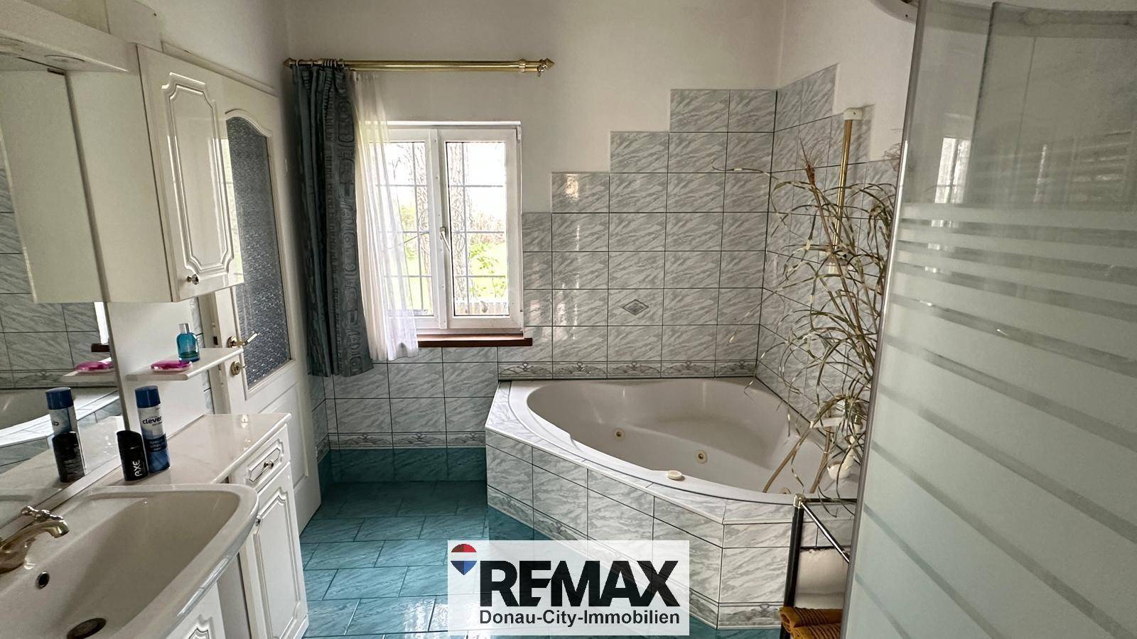 Helles Badezimmer mit Eckbadewanne, Fenster und weiß-blauen Fliesen im 80er-Jahre-Stil.