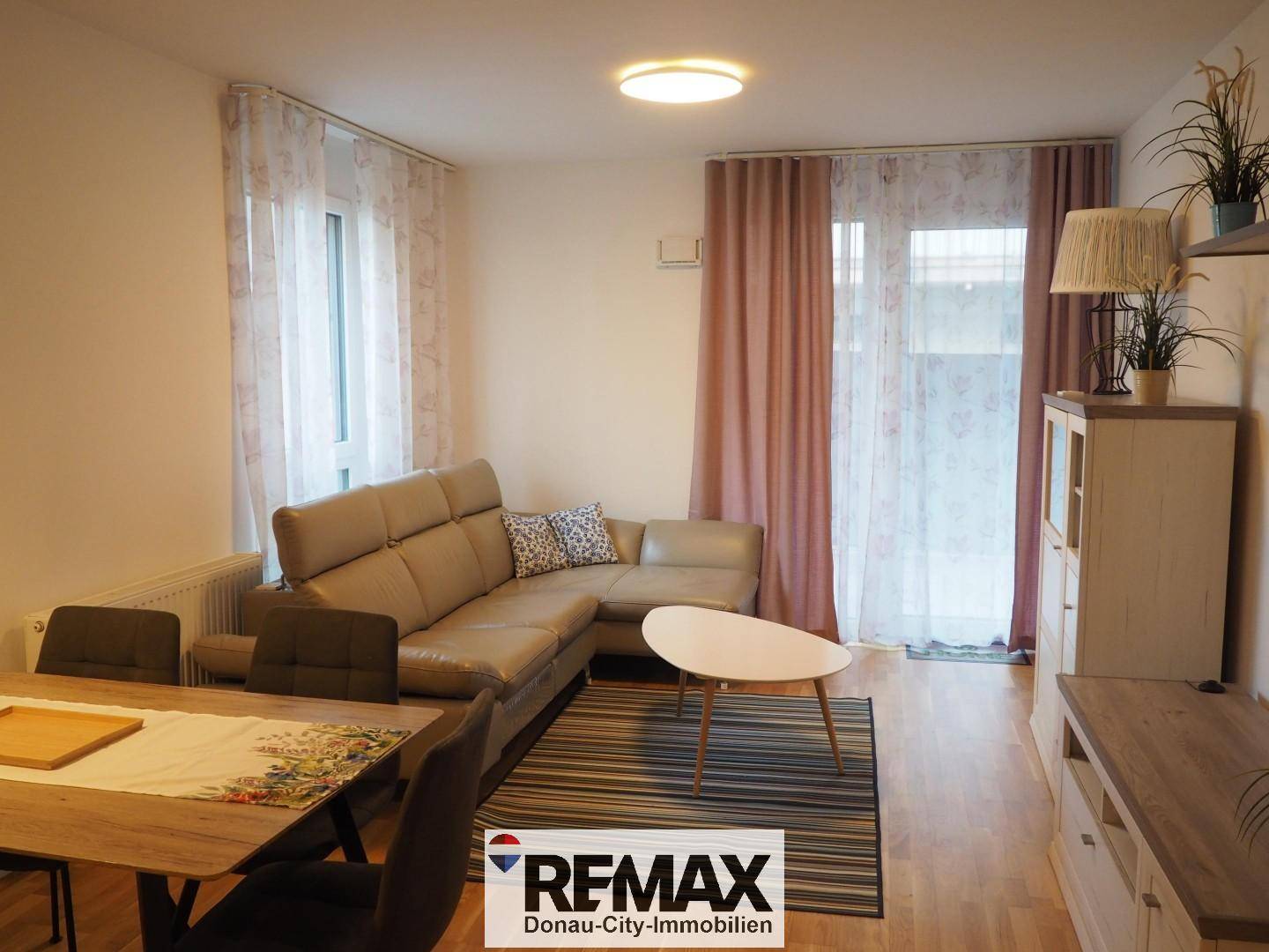 Wohnbereich mit beigem Ecksofa und Esstisch, Zugang zum Balkon durch große Fenster.