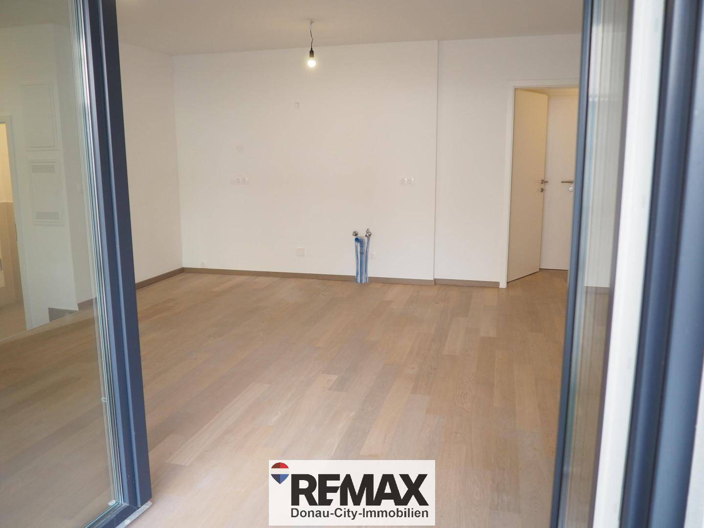 Leerer Raum mit Holzboden und Anschlüssen an der Wand, bereit für die Kücheninstallation.