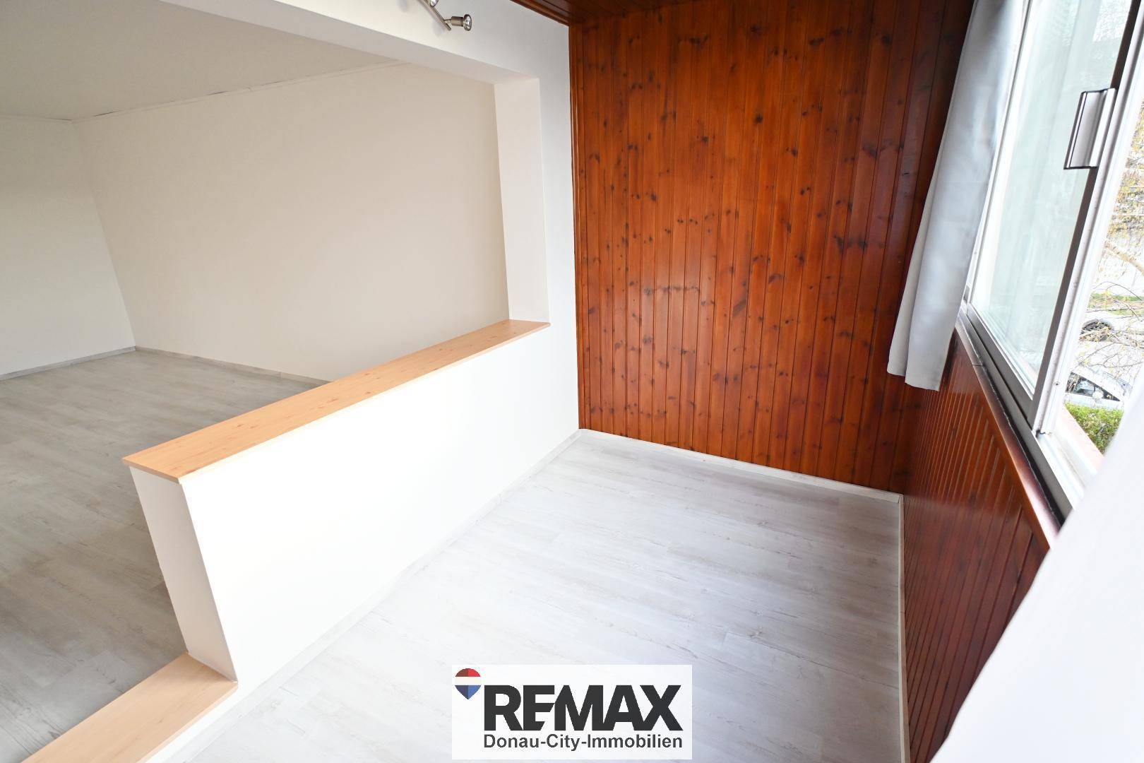 Heller, holzvertäfelter Bereich mit großen Fenstern und hellem Laminatboden.