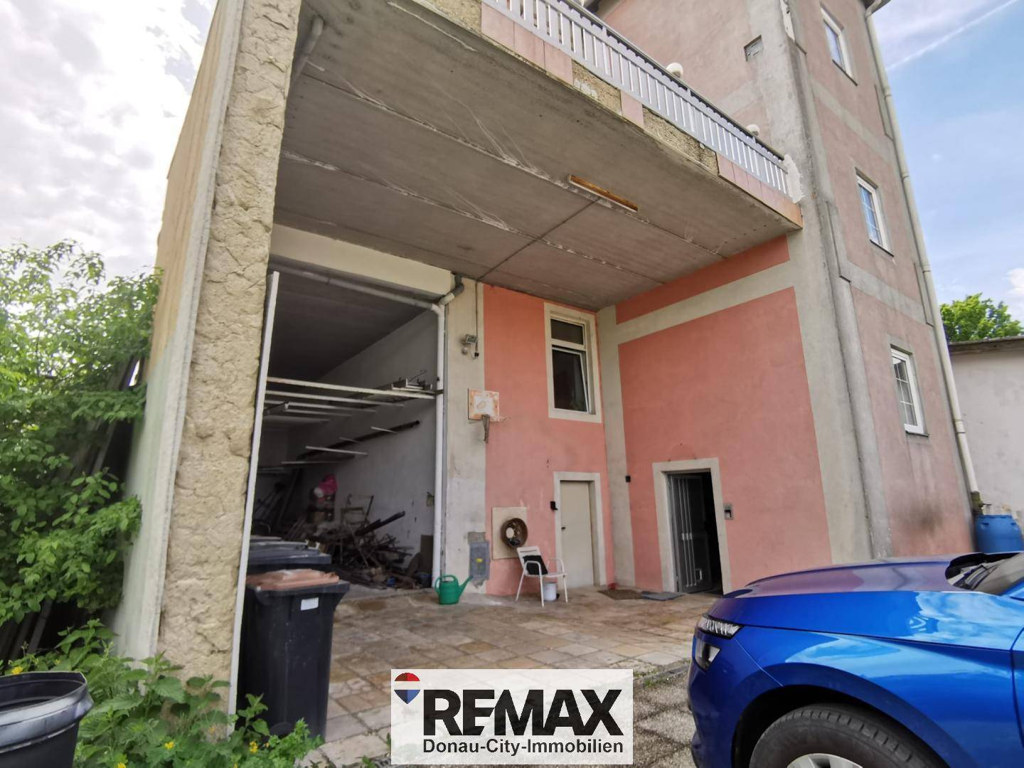 Seitenansicht des Gebäudes mit großer Garageneinfahrt, rosa Fassade und einem Auto.