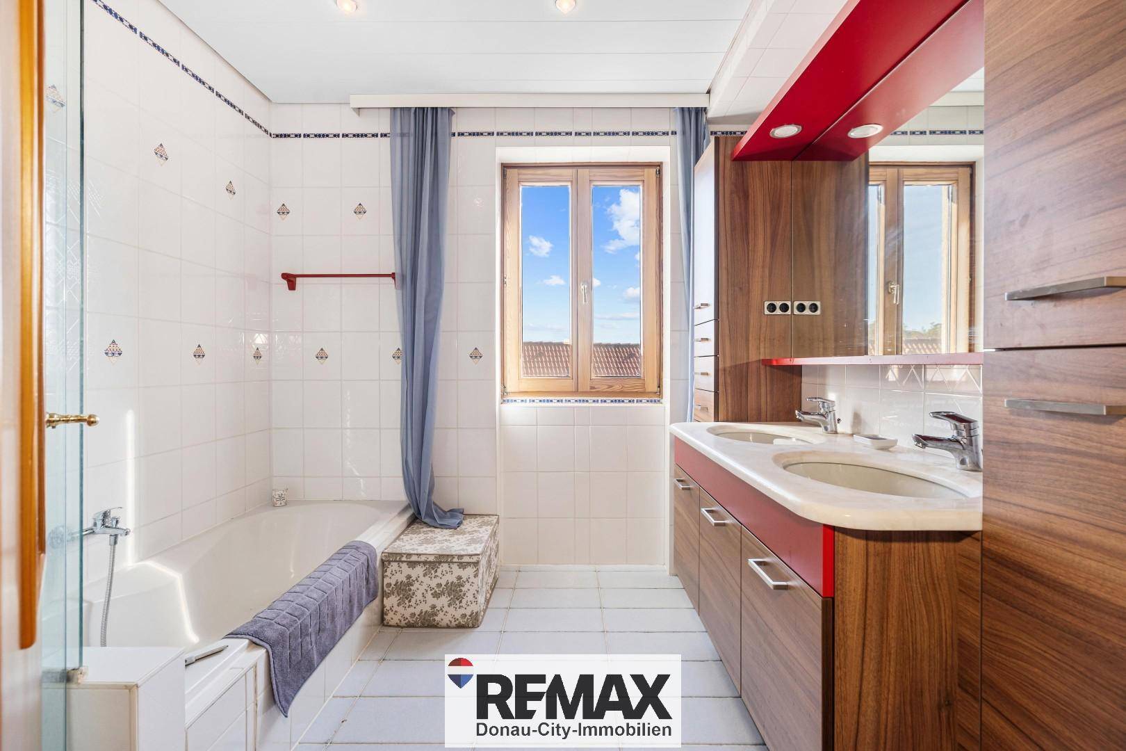 Helles Badezimmer mit Badewanne, Holzwaschtisch und Fenster.