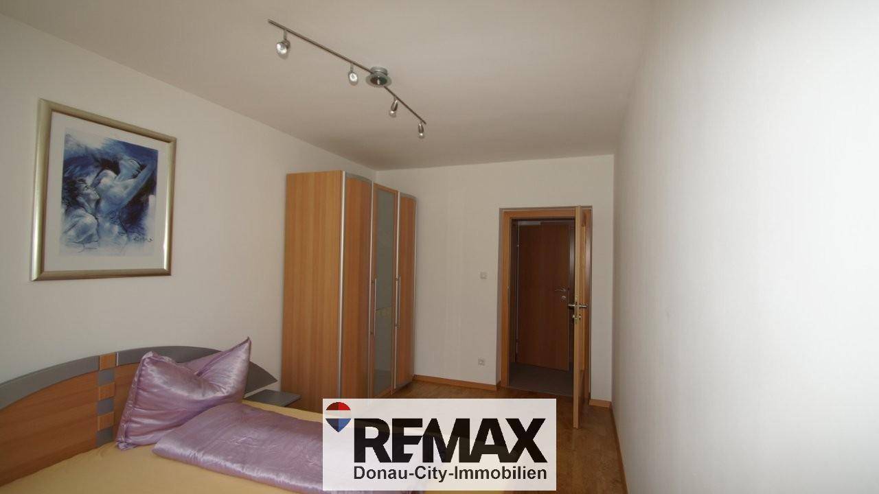 Schlafzimmer mit Bett, lila Bettwäsche und einem Holzschrank, ausgestattet mit Parkettboden.